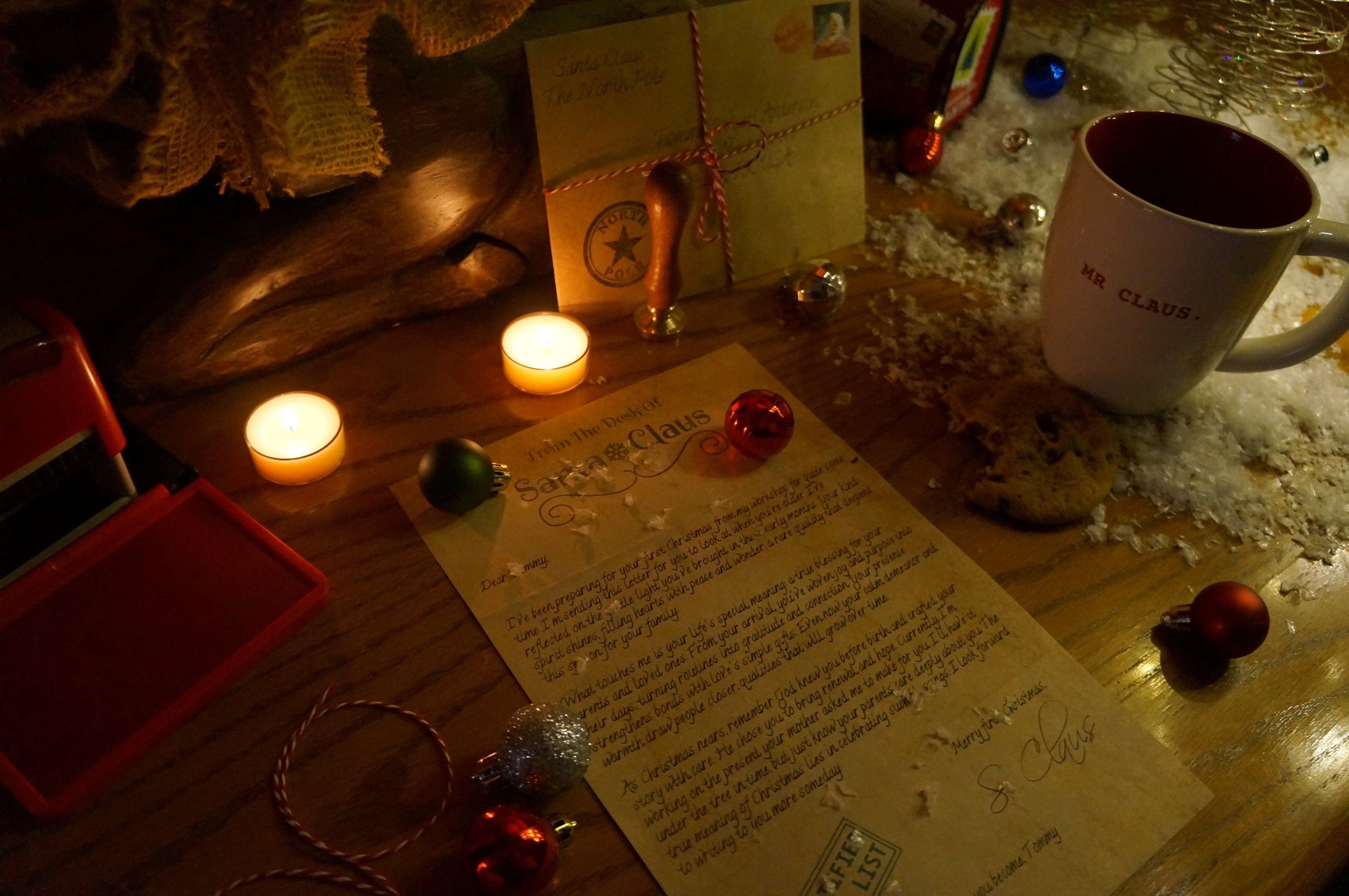 Candlelit desk with a letter, mug, and small objects on a wooden surface