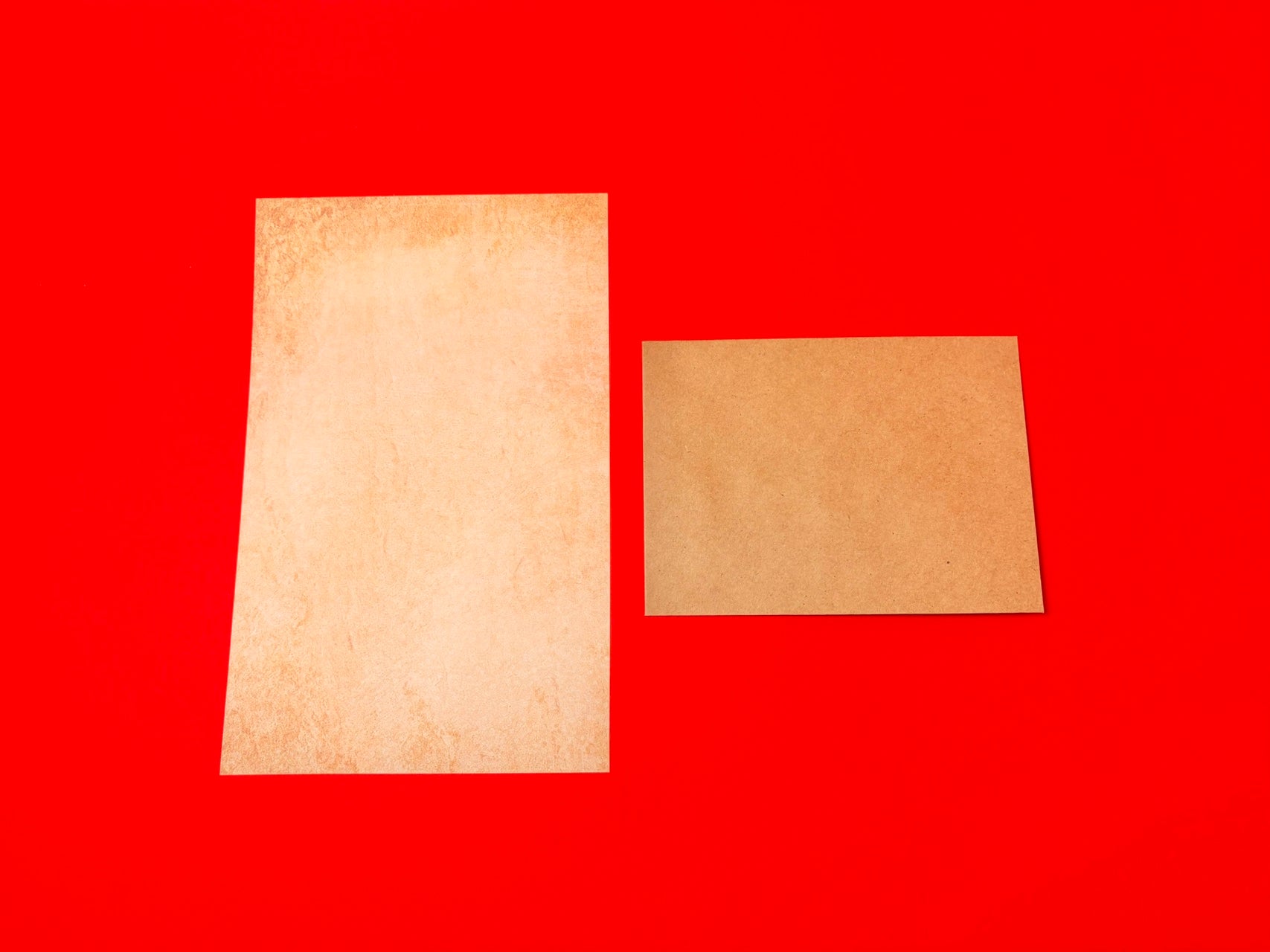Two blank textured paper cards, one tall and one wide, displayed on a solid bright red background.