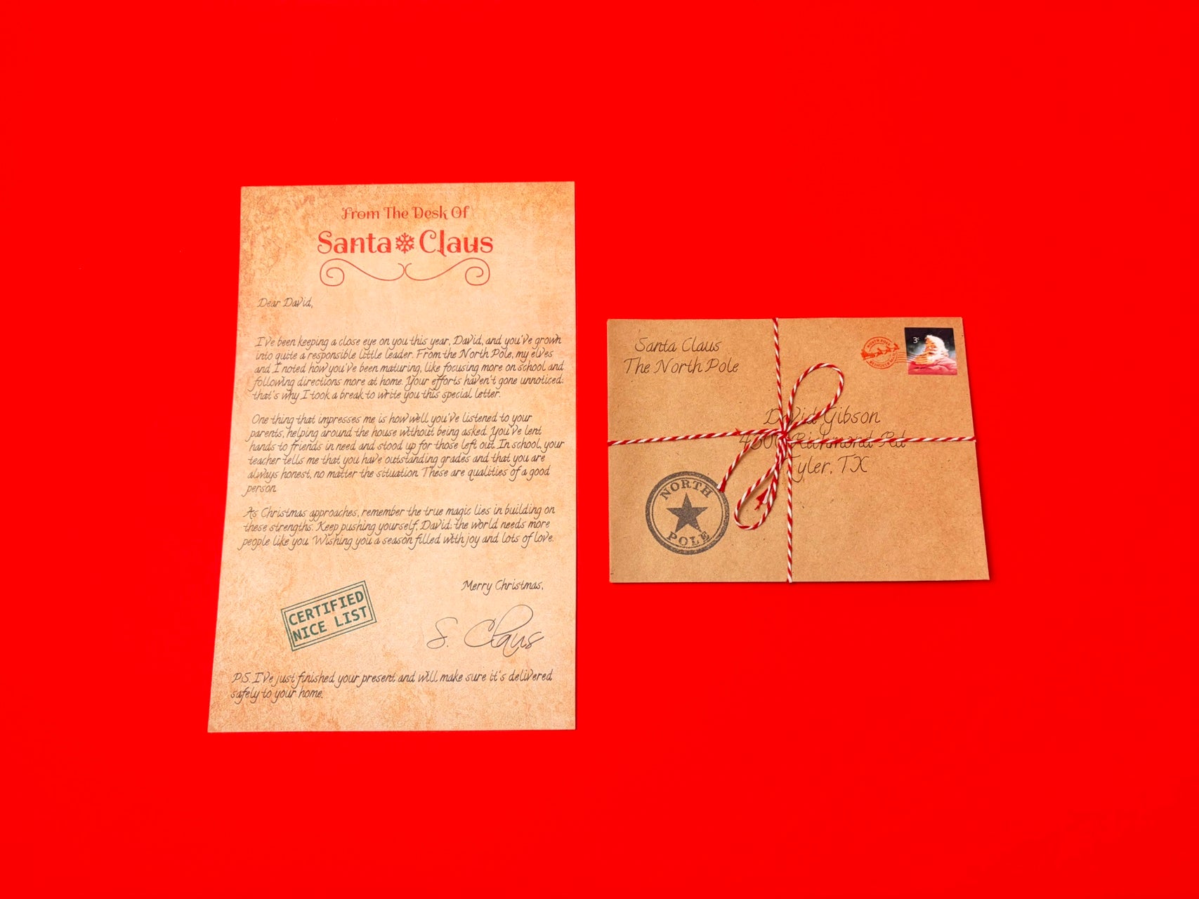 A vintage-style Christmas letter on aged beige paper next to a matching brown envelope tied with red string, set against a solid red background.